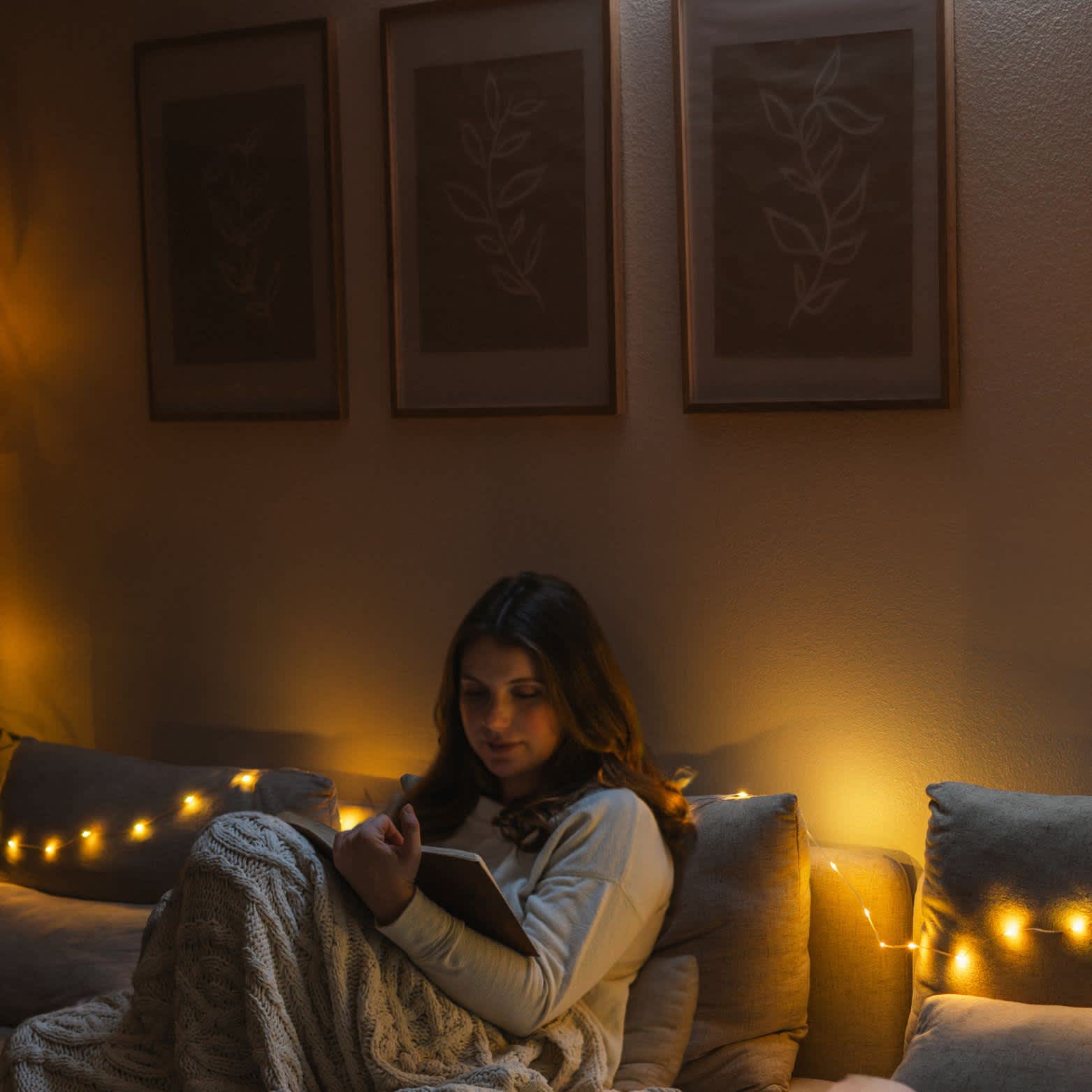 A woman reading in a living room illuminated with Solar String Lights from LuminAID.