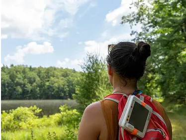 A hiker with a LuminAID lantern clipped to her backpack, charging in the sun