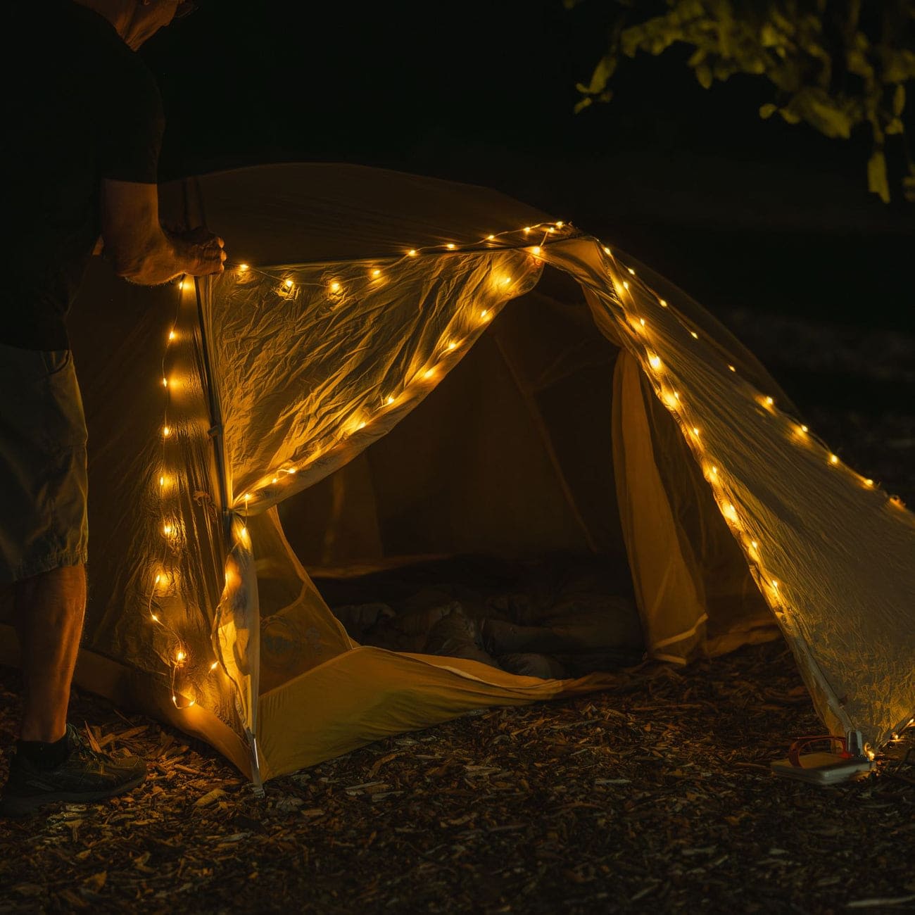 A man hanging the LuminAID Solar String Light on a tent at night, illuminating the campsite with a warm glow.