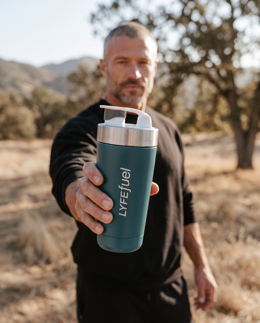 A man holding out a LyfeFuel shaker bottle outdoors
