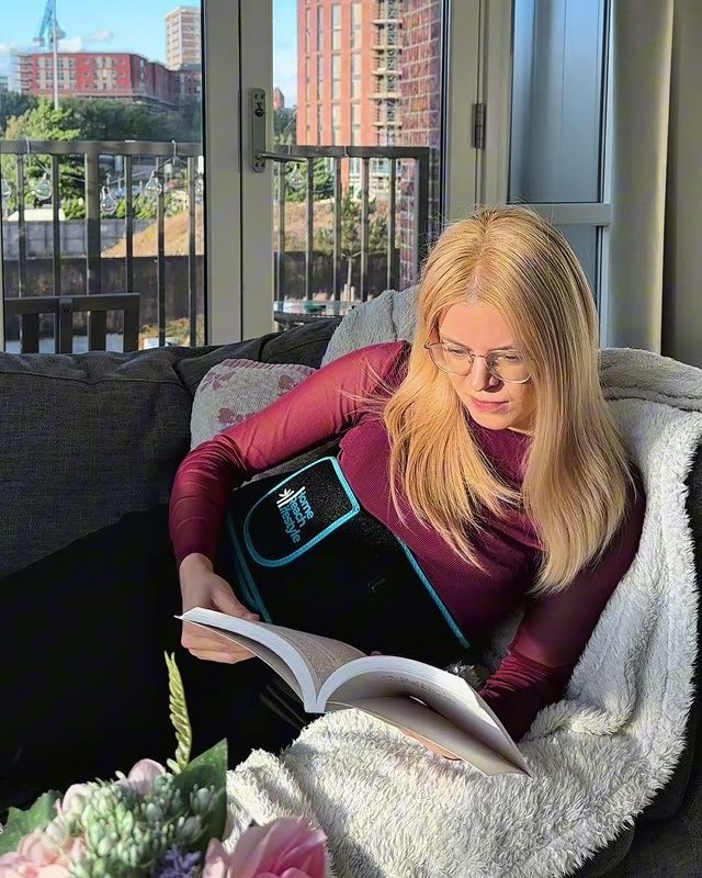 Woman reading on the couch with the ThermaLight360 Pro wrapped around her stomach