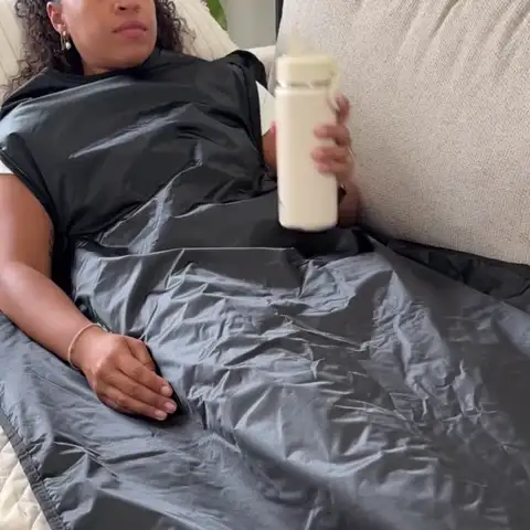 Woman relaxing on her sofa inside the FlexiHeat sauna blanket