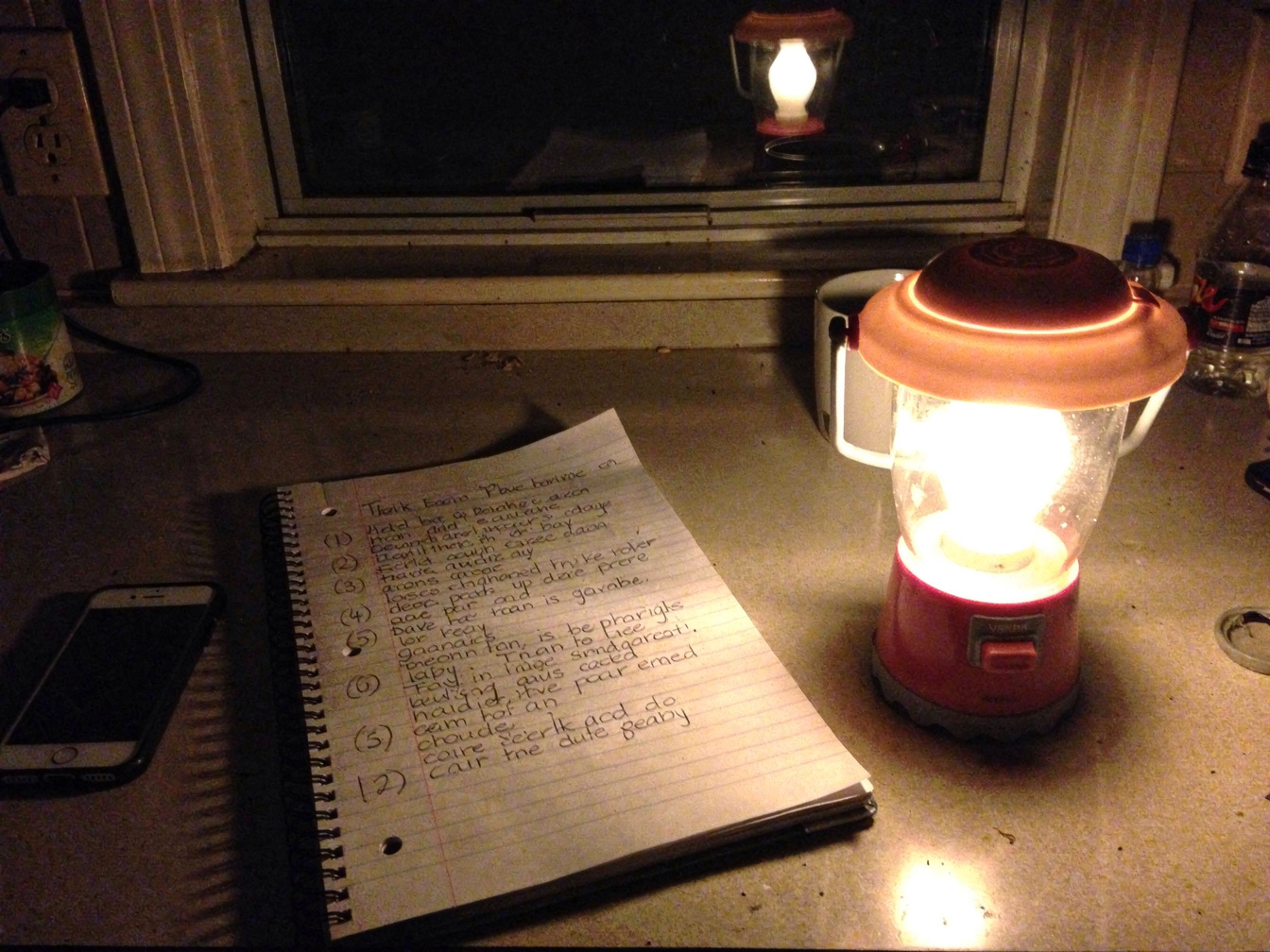 Illustration: a notebook with a handwritten list beside a lit battery lantern and a dark phone on a kitchen counter at night.
